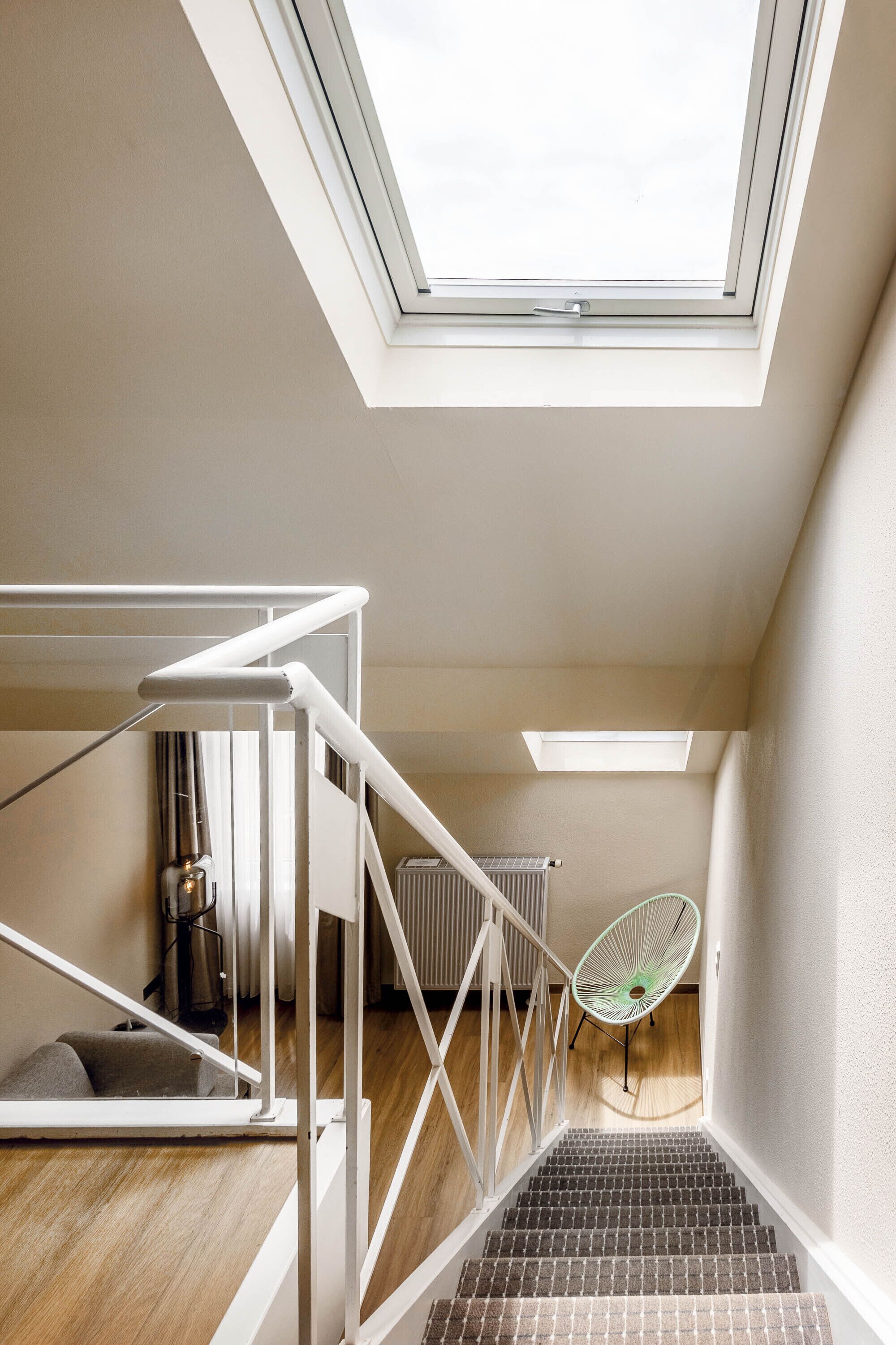 A modern loft bedroom with skylights, a staircase, and a green chair.