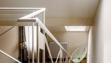 A modern loft bedroom with skylights, a staircase, and a green chair.