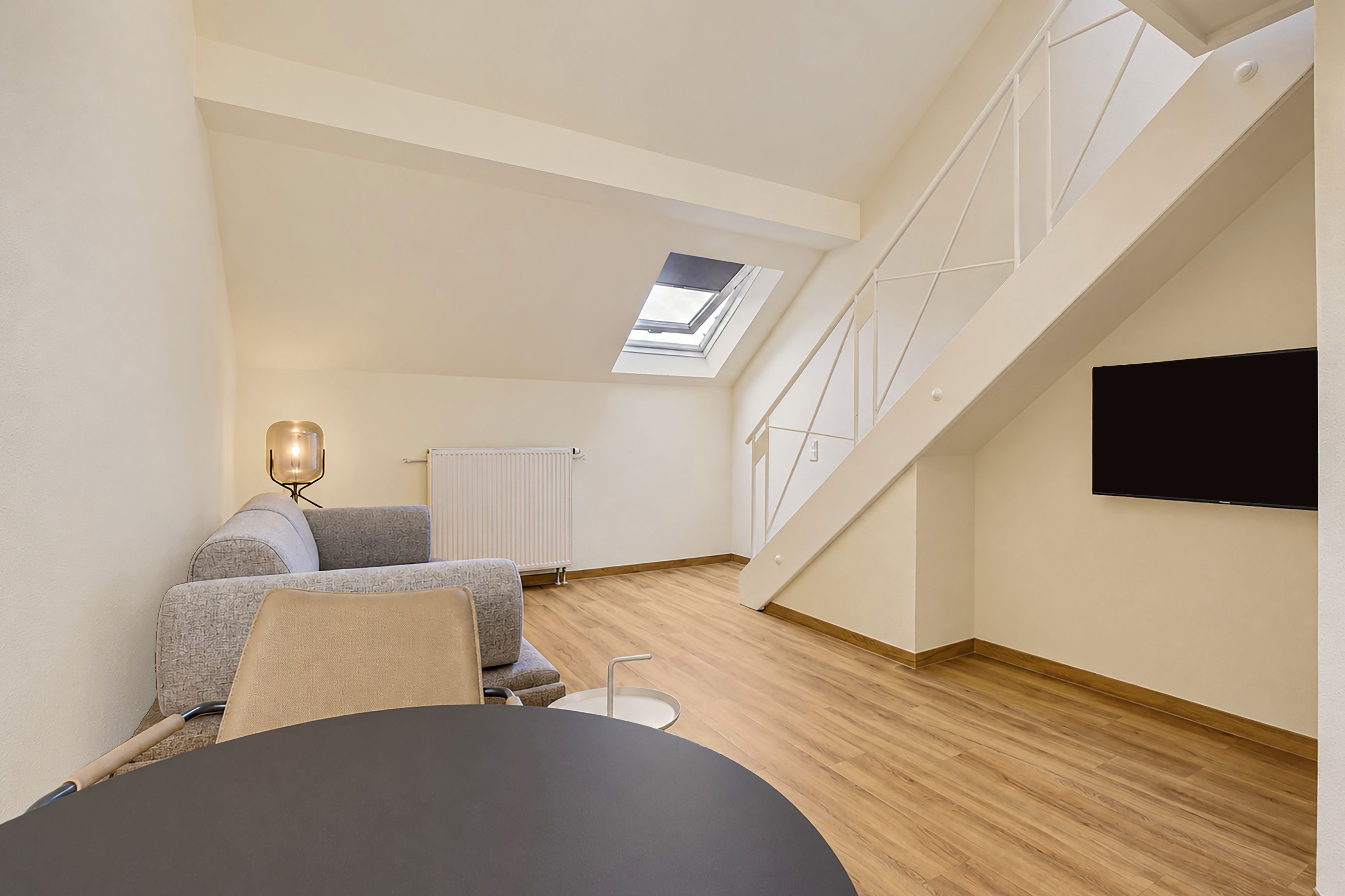 Una sala de estar moderna con un sofá, una mesa, una lámpara y un televisor montado en la pared.