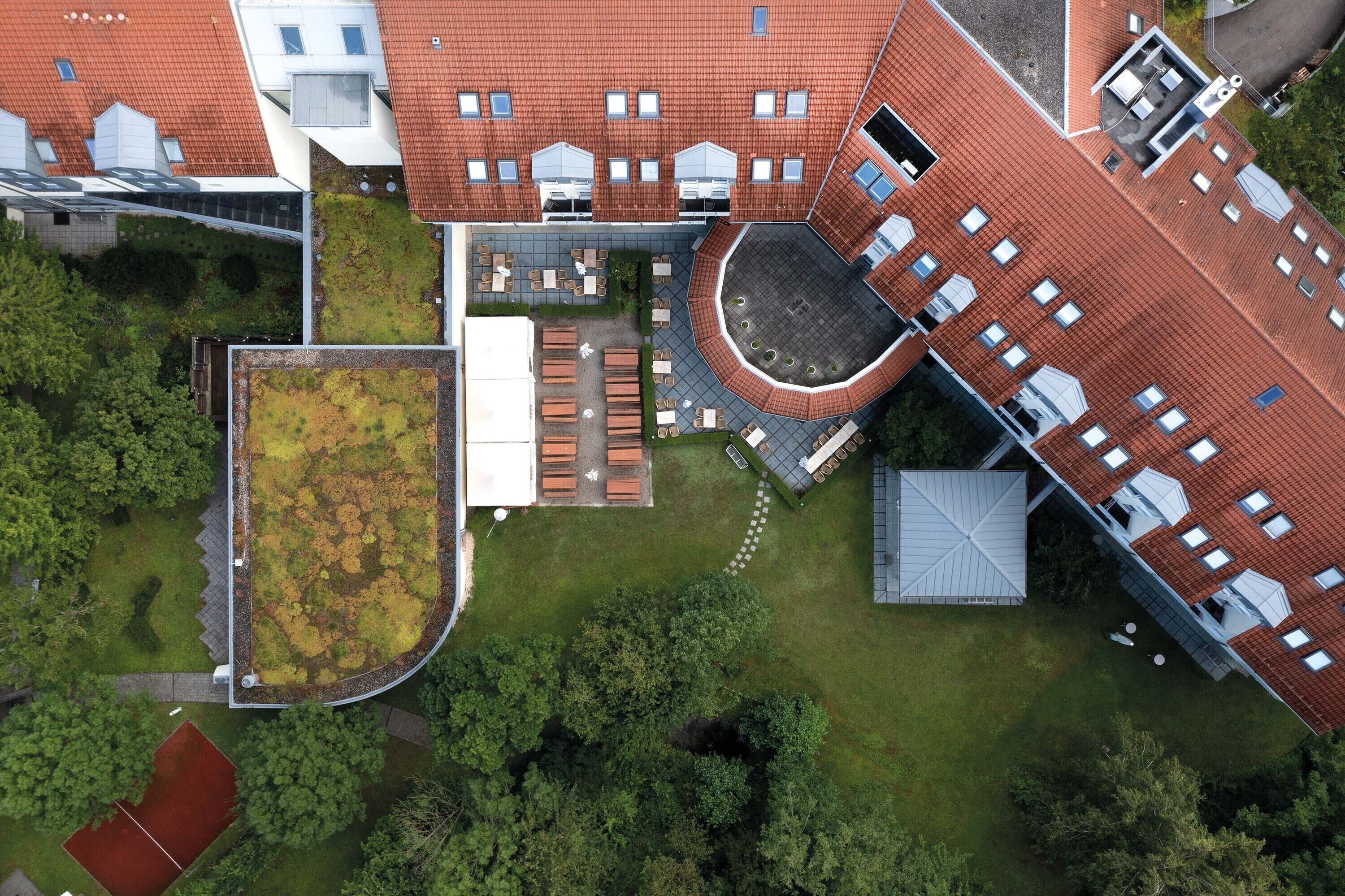 An aerial view of a building with a red-tiled roof, a rooftop garden, and a circular courtyard with seating.