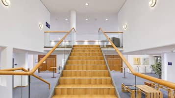 Una escalera con escalones de madera y barandillas de cristal, que sube a un piso superior.