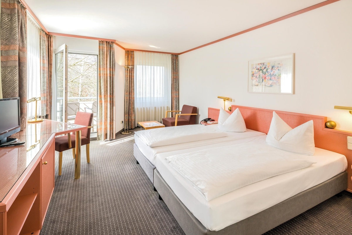 A hotel room with a bed, desk, chair, and a view of the outdoors.