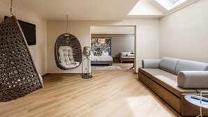 A modern living room with a hanging chair, a sofa, a small table, and a bed in the background. - Seminaris Hotel Bad Boll (Bad Boll)