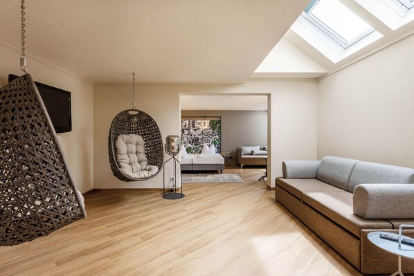 A modern living room with a hanging chair, a sofa, a small table, and a bed in the background.