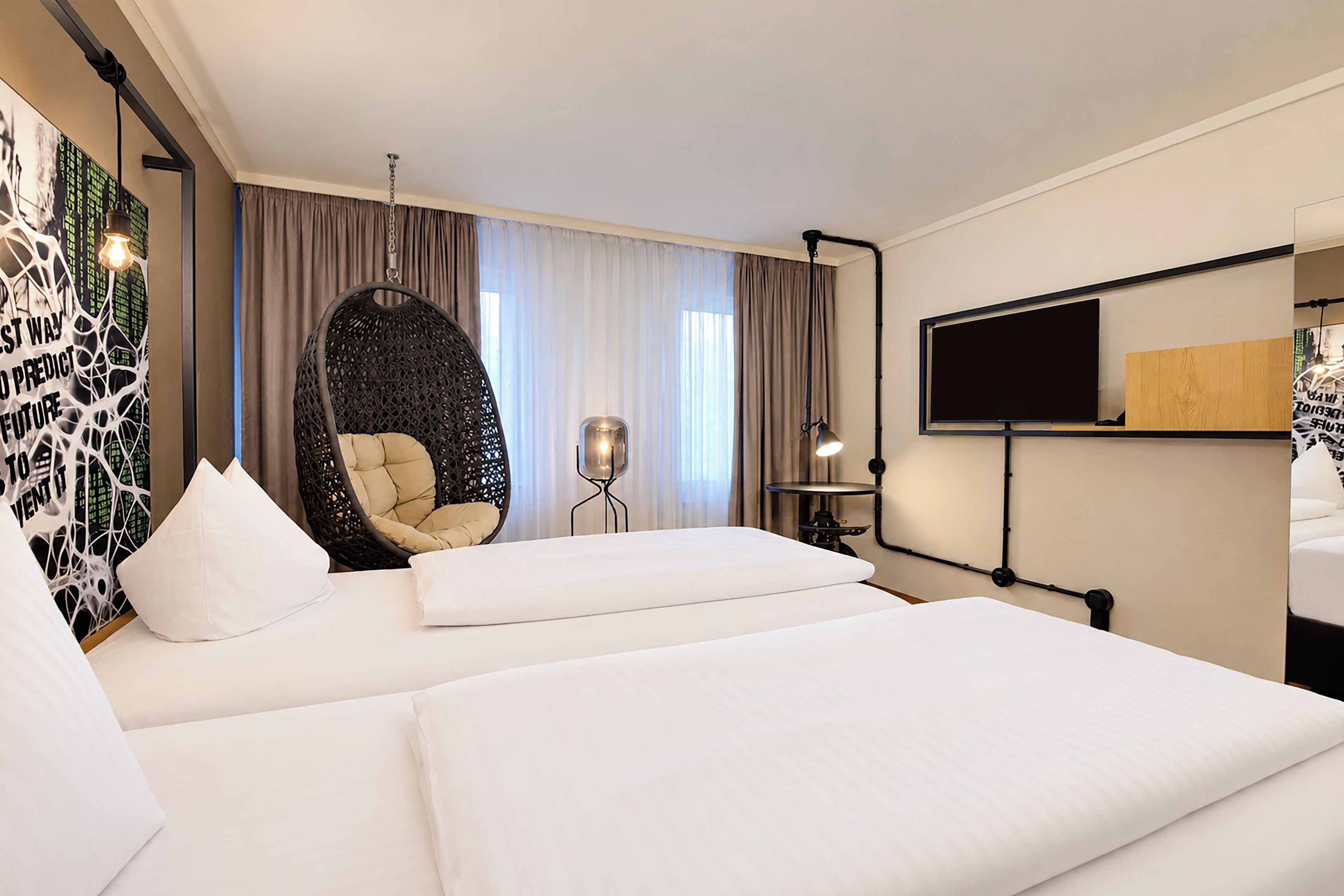 Ein Hotelzimmer mit einem großen Bett, einem Hängekorbsessel, einem Schreibtisch mit Stuhl und einem an der Wand montierten Fernseher.