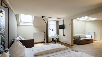 Une chambre moderne comprenant un lit, un bureau, une chaise, un canapé et un téléviseur. Elle est dotée de fenêtres de toit et d’une fenêtre qui laissent entrer la lumière naturelle.