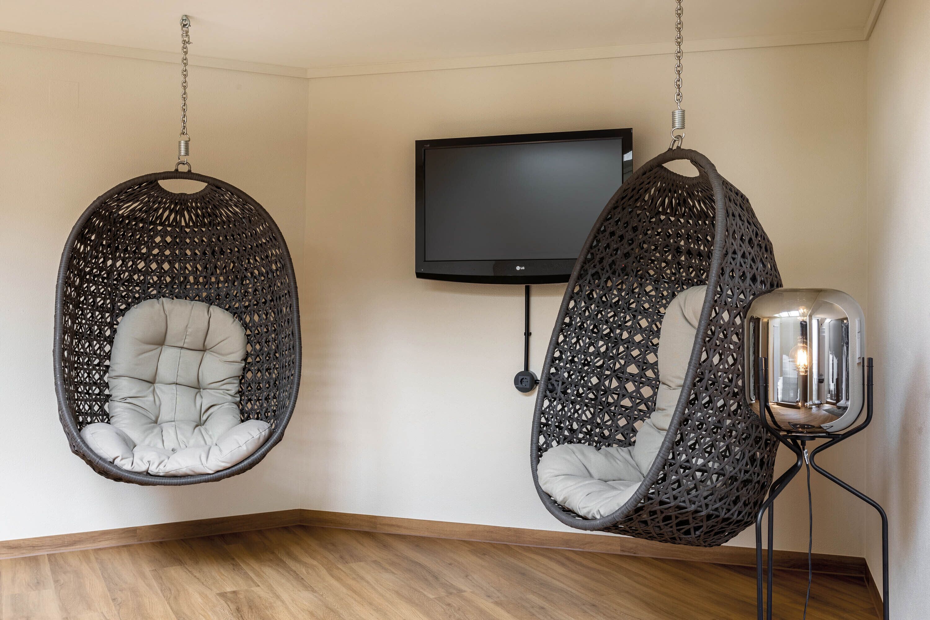 Une pièce avec deux fauteuils suspendus, un téléviseur à écran plat et une lampe sur pied.