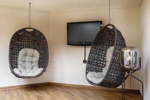 A room with two hanging chairs, a flat-screen TV, and a floor lamp. - Seminaris Sunday Hotel Bad Boll (Bad Boll)