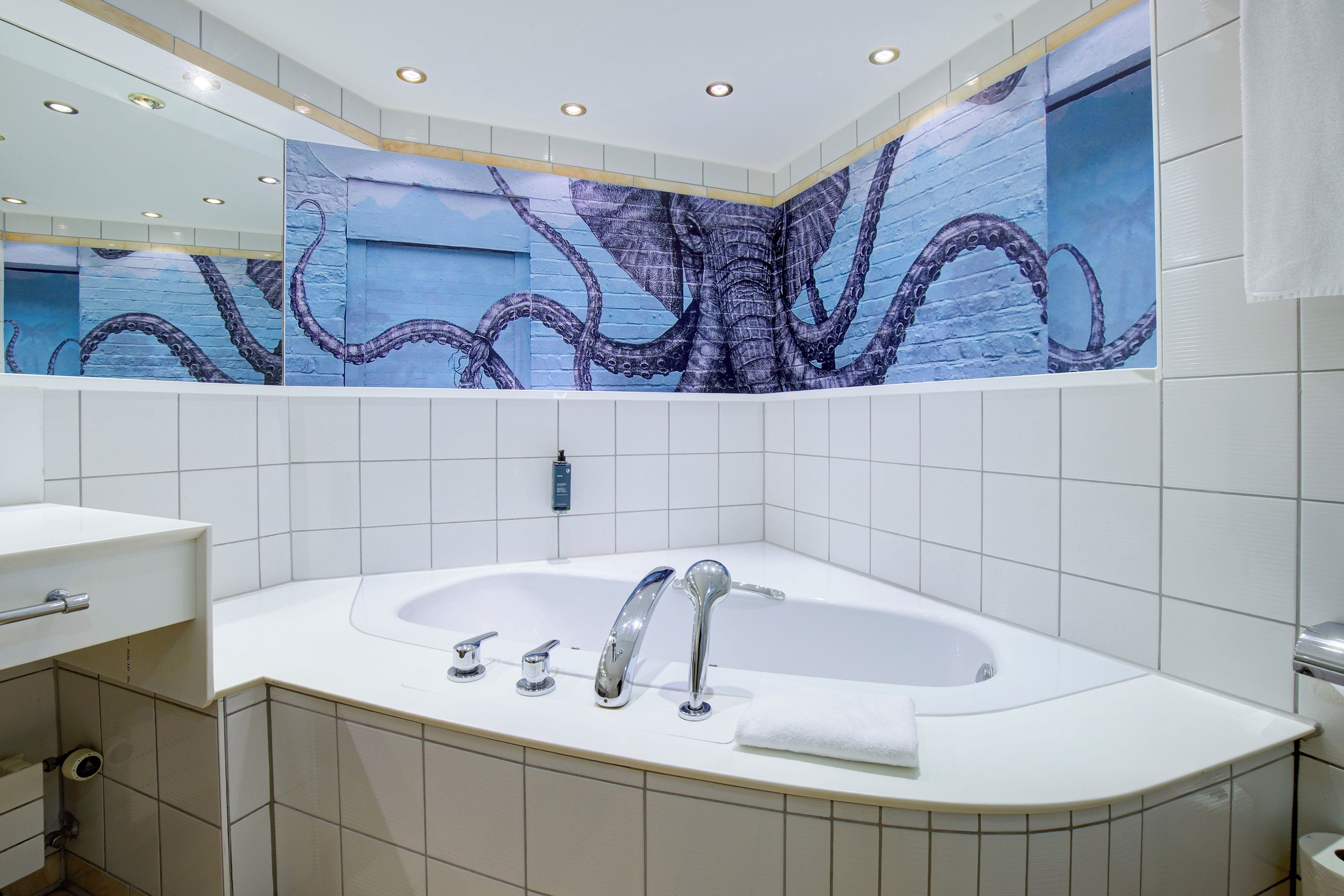 Une salle de bain moderne avec une grande baignoire, un miroir et une fresque murale représentant des tentacules de poulpe.