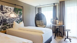 A hotel room with two beds, a hanging chair, a desk with a lamp, and a large abstract painting on the wall. - Seminaris Hotel Bad Boll (Bad Boll)