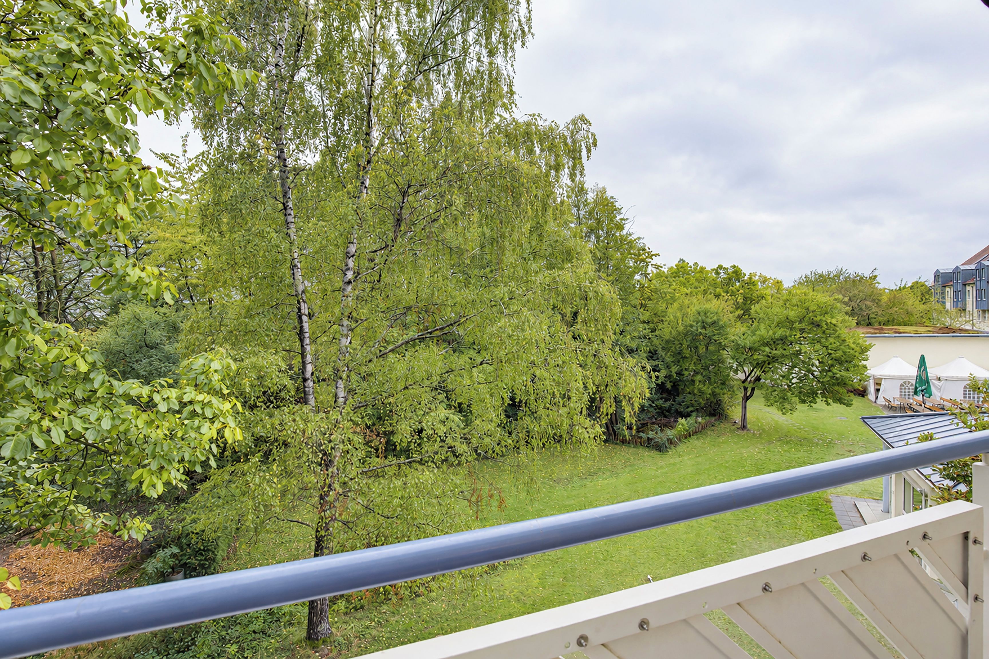 Ein Balkon mit Blick auf einen üppigen Garten und ein Gebäude mit blauem Dach.