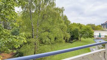 Ein Balkon mit Blick auf einen üppigen Garten und ein Gebäude mit blauem Dach.