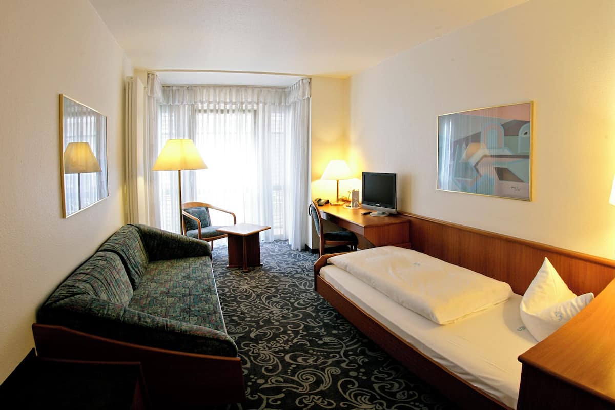 A hotel room with a bed, a sofa, a desk with a computer, a chair, and a TV.