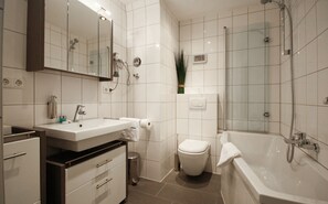 A modern bathroom with a large mirror, a sink, a toilet, and a bathtub. - Alfa Hotel (Karlsruhe)