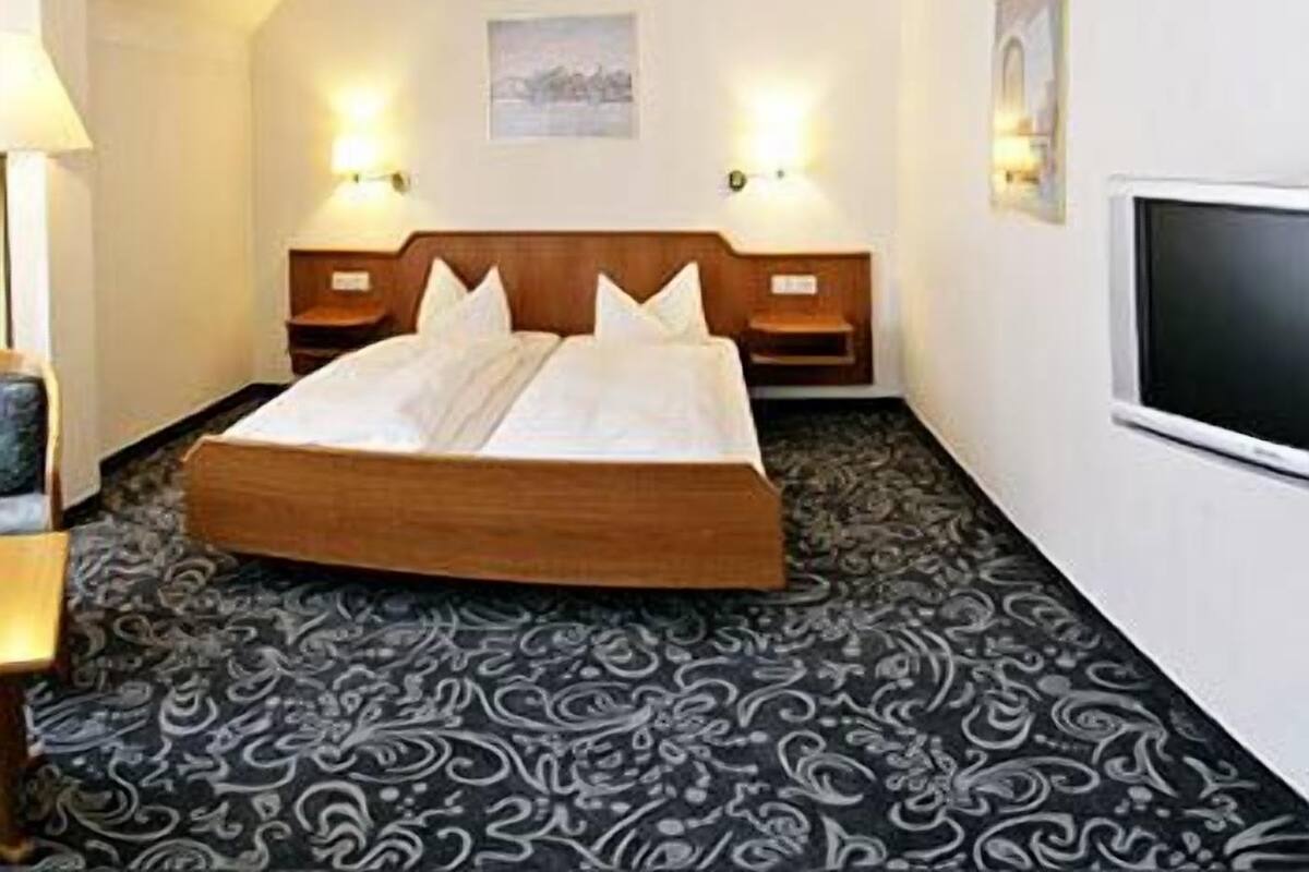 A hotel room with a large bed, two bedside tables, a flat-screen TV, and patterned carpet.
