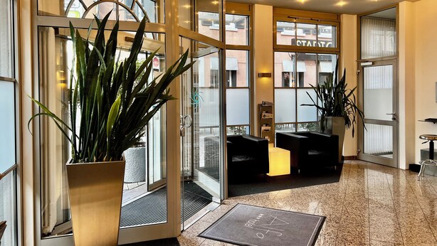 A hotel lobby with a reception desk, seating area, and large windows. - Alfa Hotel (Karlsruhe)