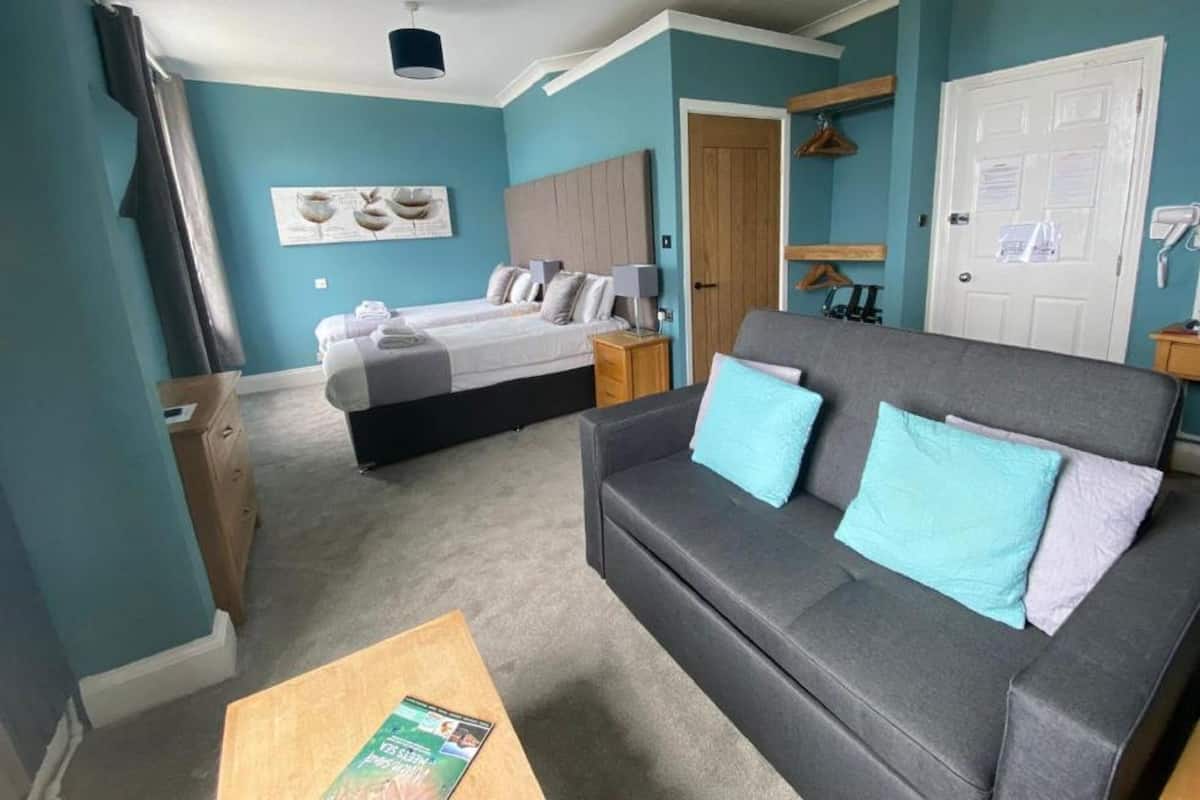 A room with two beds, a sofa, a wooden dresser, a coat rack, and a door with a towel hanging on it.