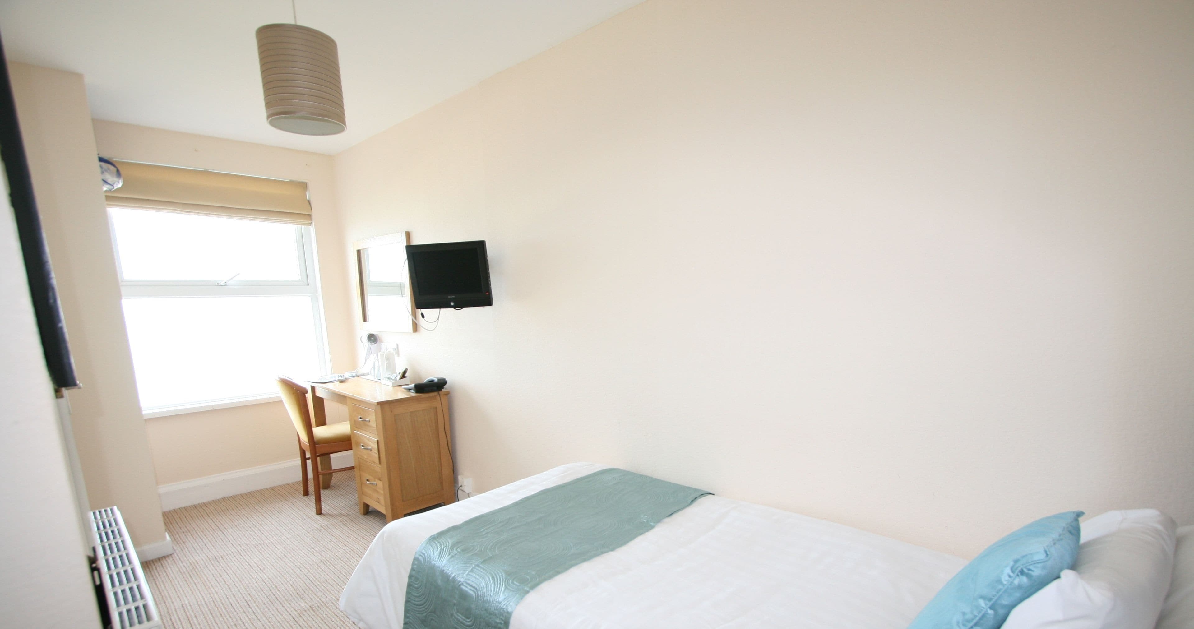 Une chambre d’hôtel avec un lit, un bureau, une chaise, une télévision et une fenêtre.
