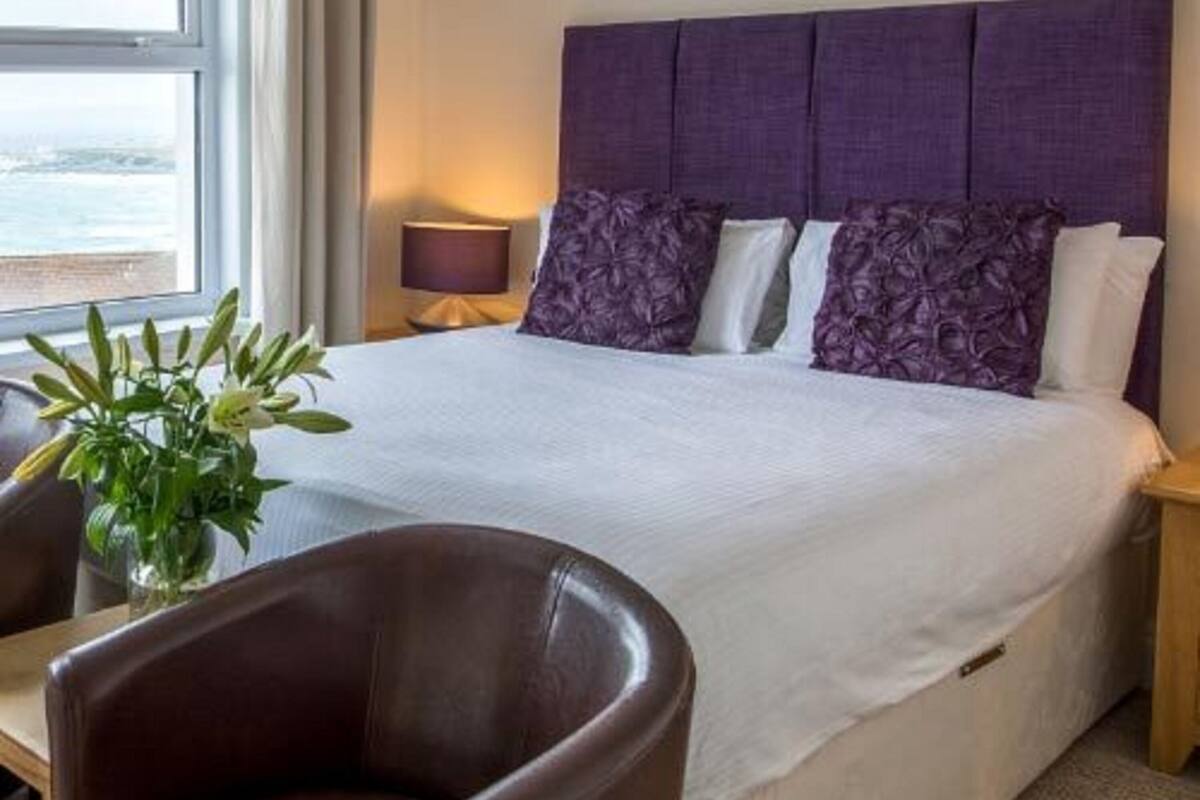 A hotel room with a large bed, a chair, a nightstand, and a window with curtains.