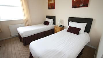 A hotel room with two single beds, a bedside table with a lamp, and a radiator.