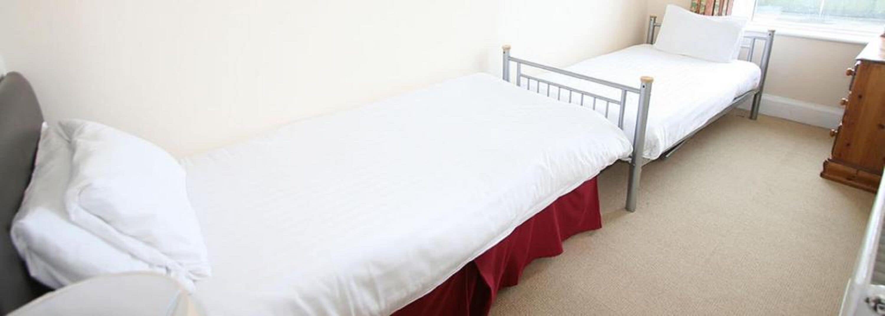 A single-bed room with a metal frame, white bedding, and a red skirted bed base.