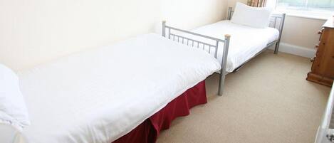 Quarto individual com cama de estrutura metálica, roupa de cama branca e base estofada vermelha.