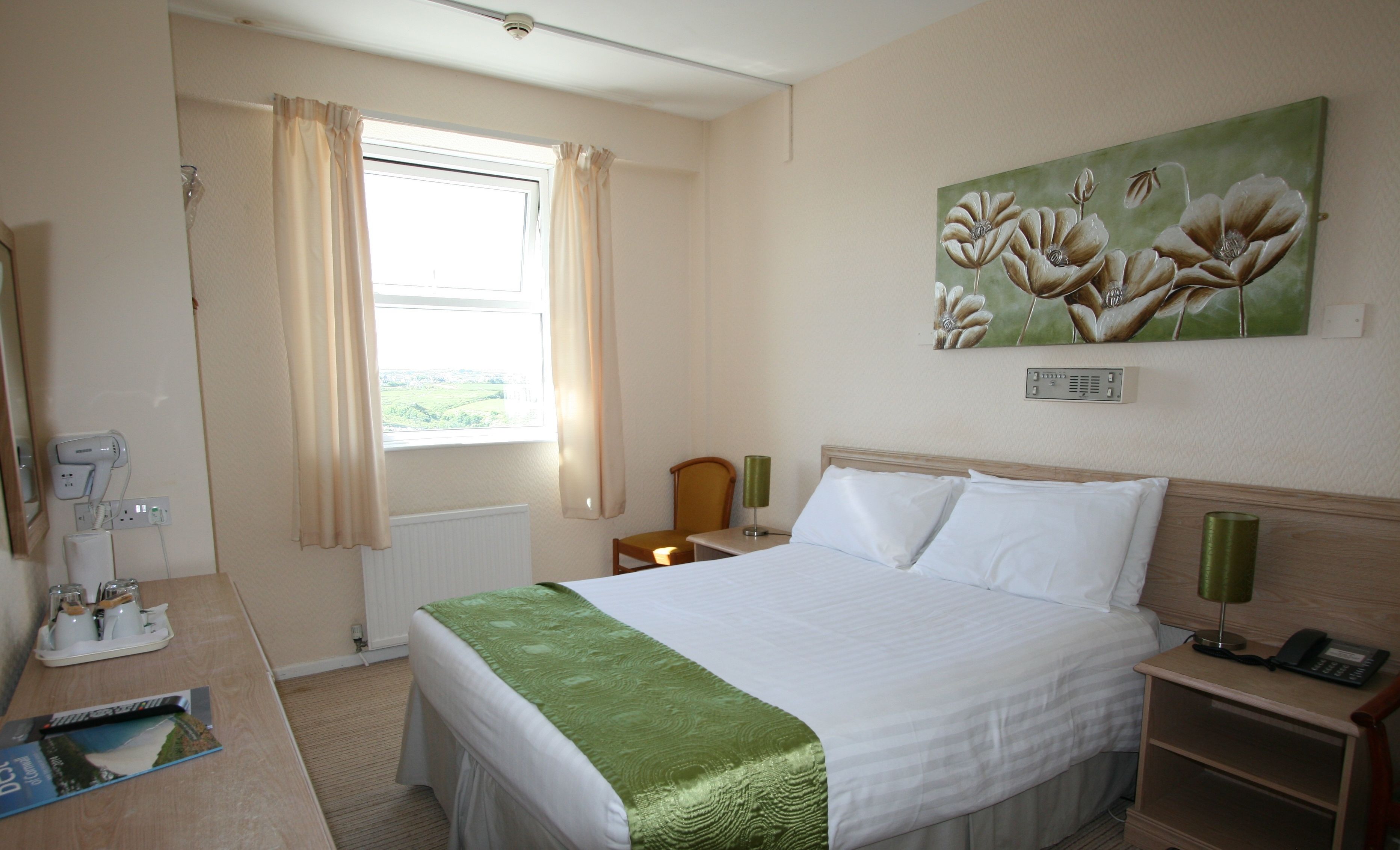 A hotel room with a bed, a desk with a telephone, a lamp, and a painting on the wall.