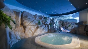 A spa area with a hot tub, rock walls, and a ceiling with star-like lights. - Hotel Vesna (Šoštanj)