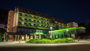 A multi-story hotel with a green and beige facade, a visible entrance, and a landscaped area with plants in front. - Hotel Vesna (Šoštanj)