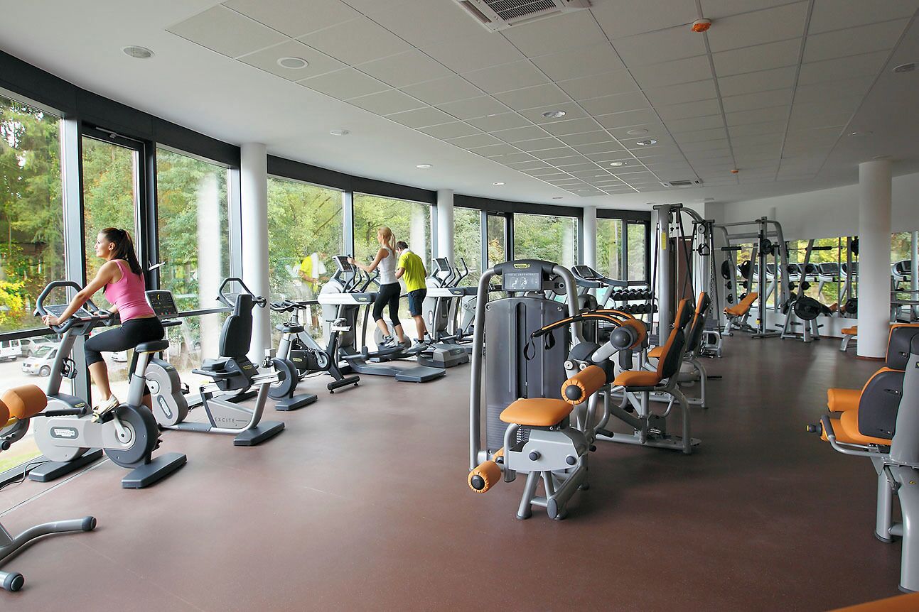 Un gimnasio con diversas máquinas de ejercicio, ventanas amplias y un diseño espacioso.