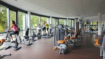 Un gimnasio con diversas máquinas de ejercicio, ventanas amplias y un diseño espacioso.