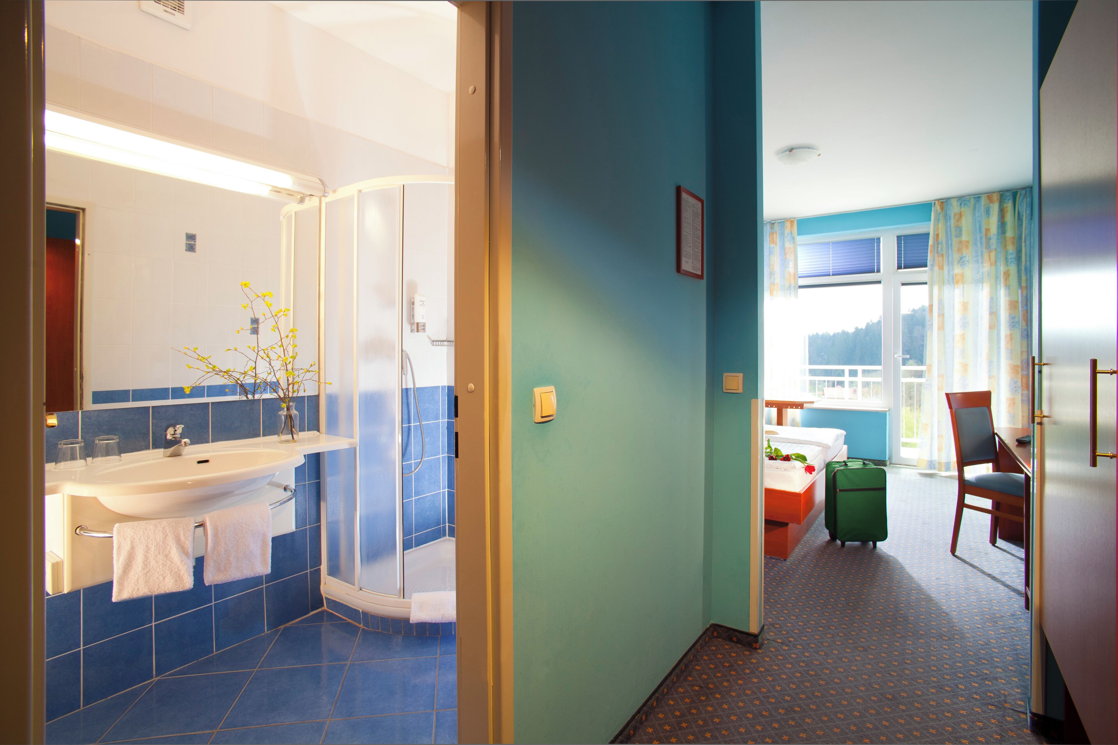 Una habitación de hotel con baño, ducha, cama, una silla y una maleta.