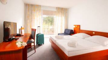 Une chambre d’hôtel avec un lit en bois, un bureau avec une chaise, une télévision et une valise.