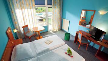 A hotel room with two beds, a desk with a TV, a chair, a small table, and a window with curtains.