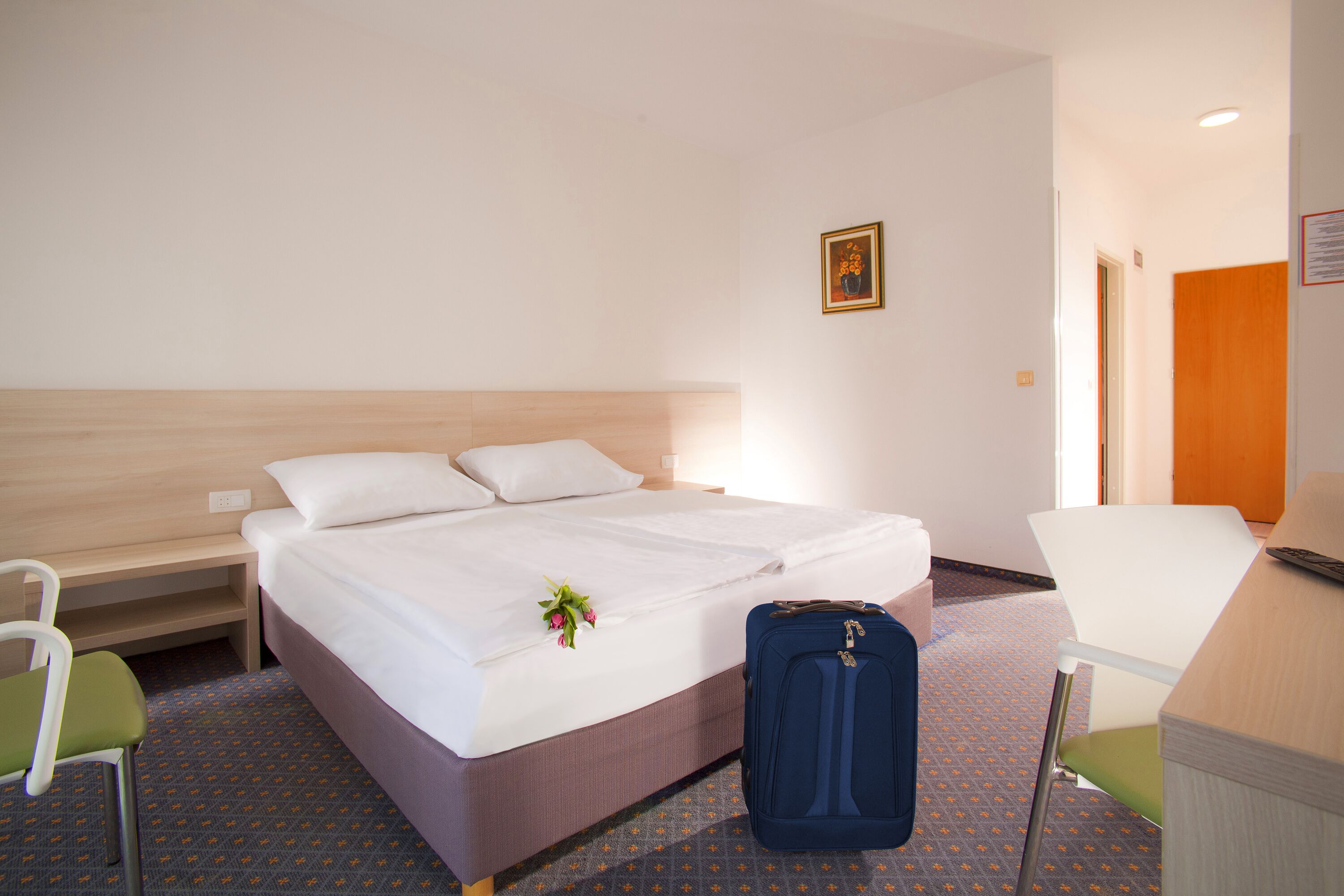 Ein Hotelzimmer mit Bett, Schreibtisch, Stuhl und Koffer.