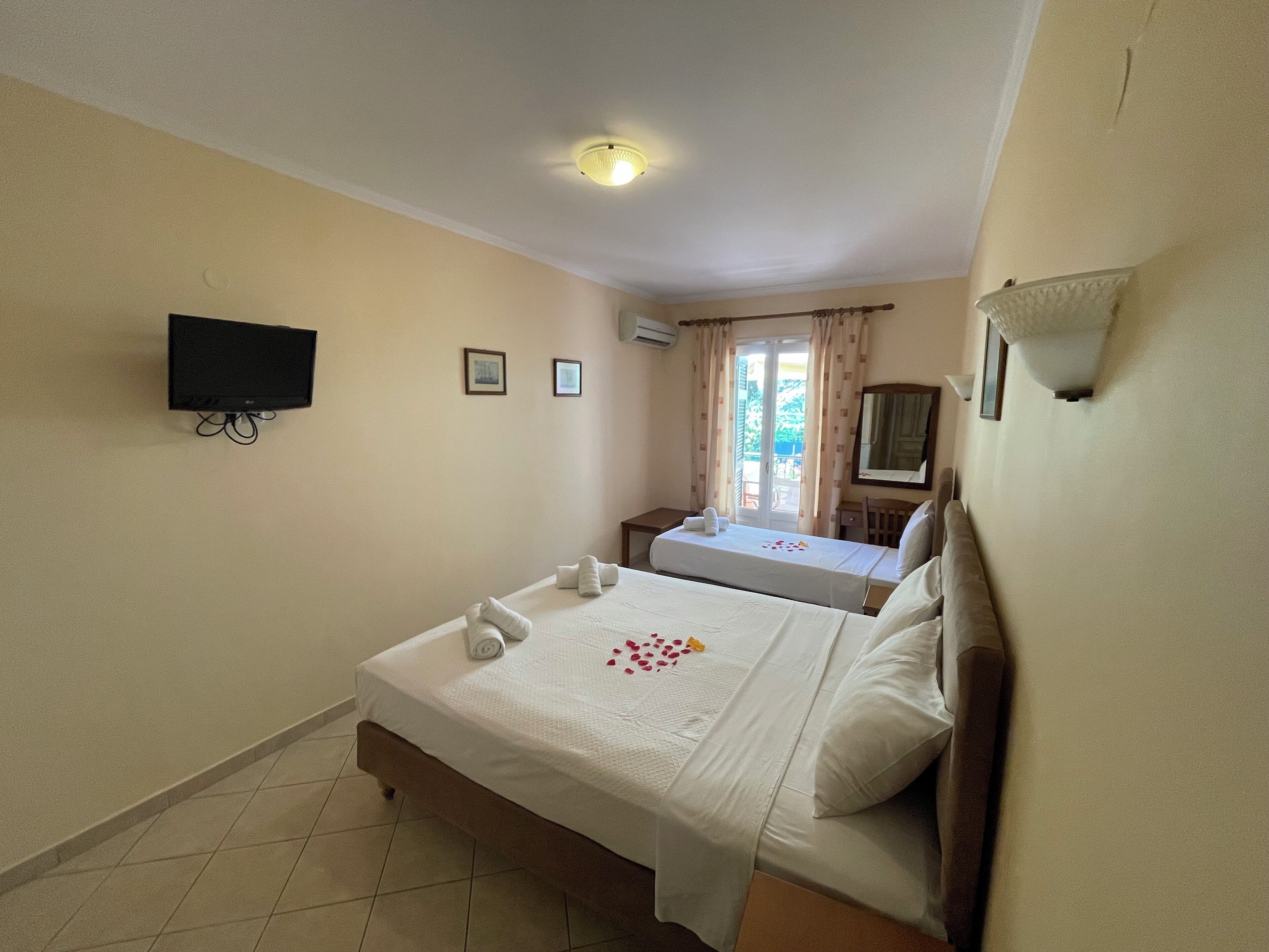 A hotel room with two beds, a television, and a window with curtains.