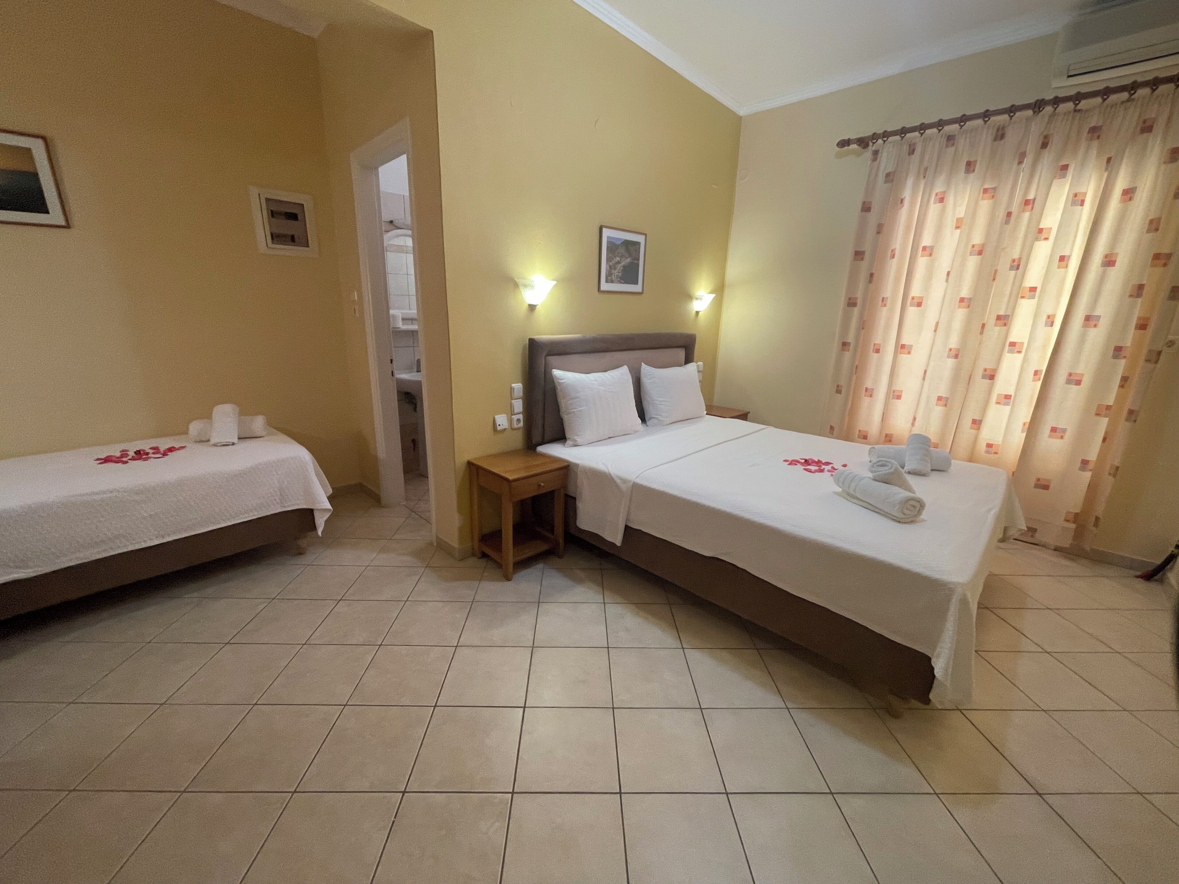 A hotel room with two single beds, a larger bed, a nightstand, and a bathroom visible through an open door.