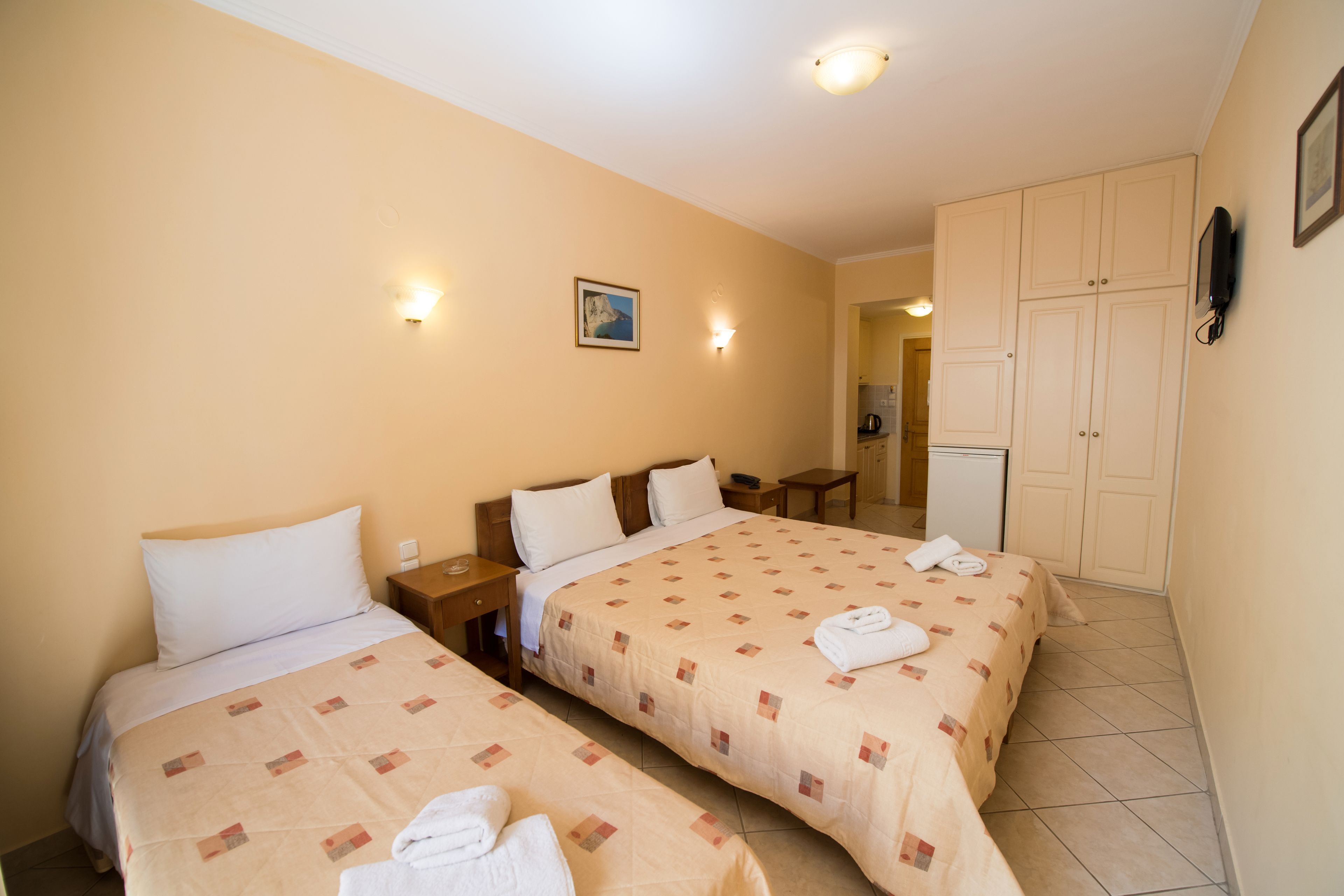 A hotel room with two beds, a small desk, a nightstand, and a wall-mounted TV.