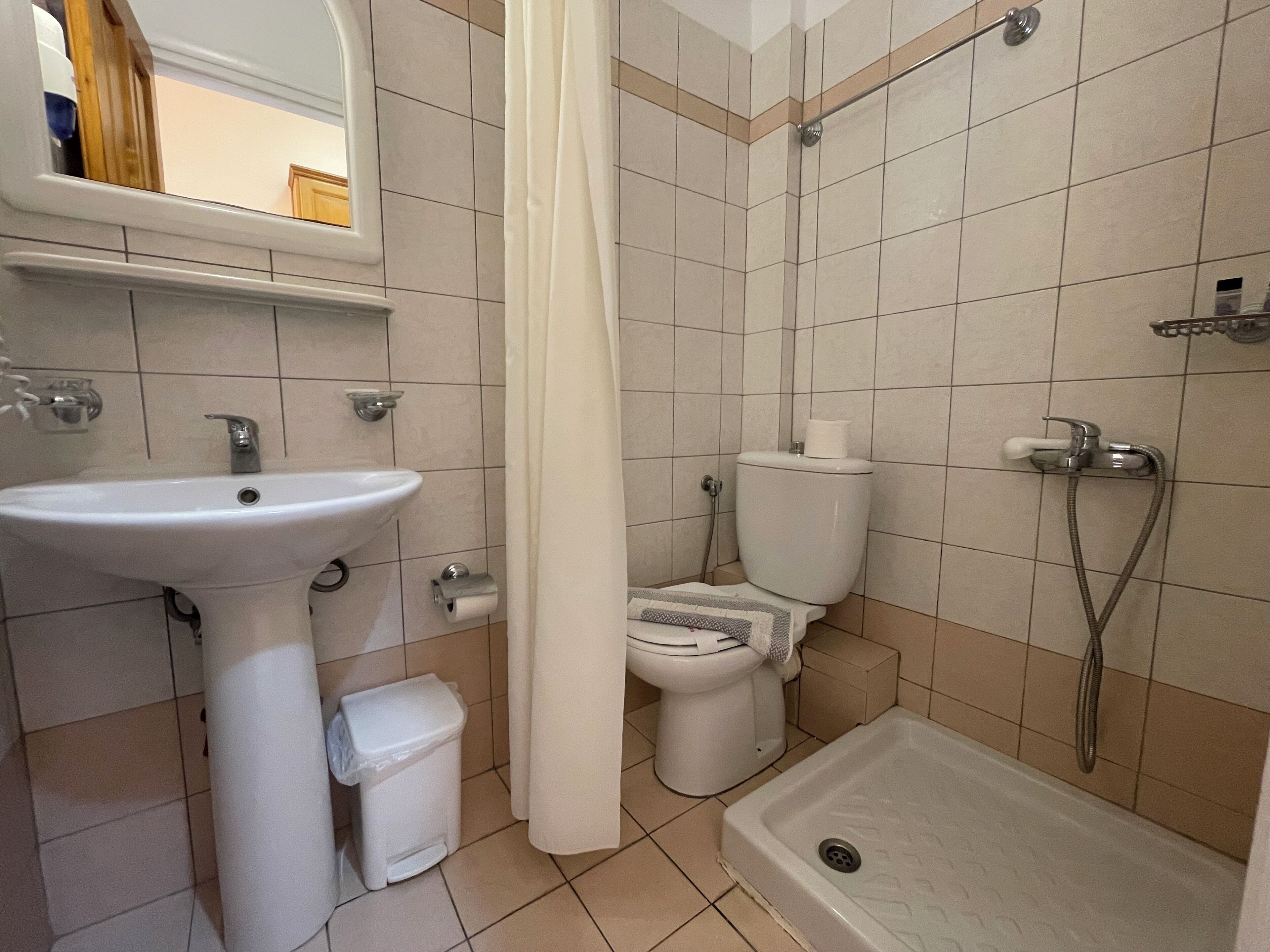 Un baño con lavamanos, inodoro, ducha y un pequeño cubo de basura.