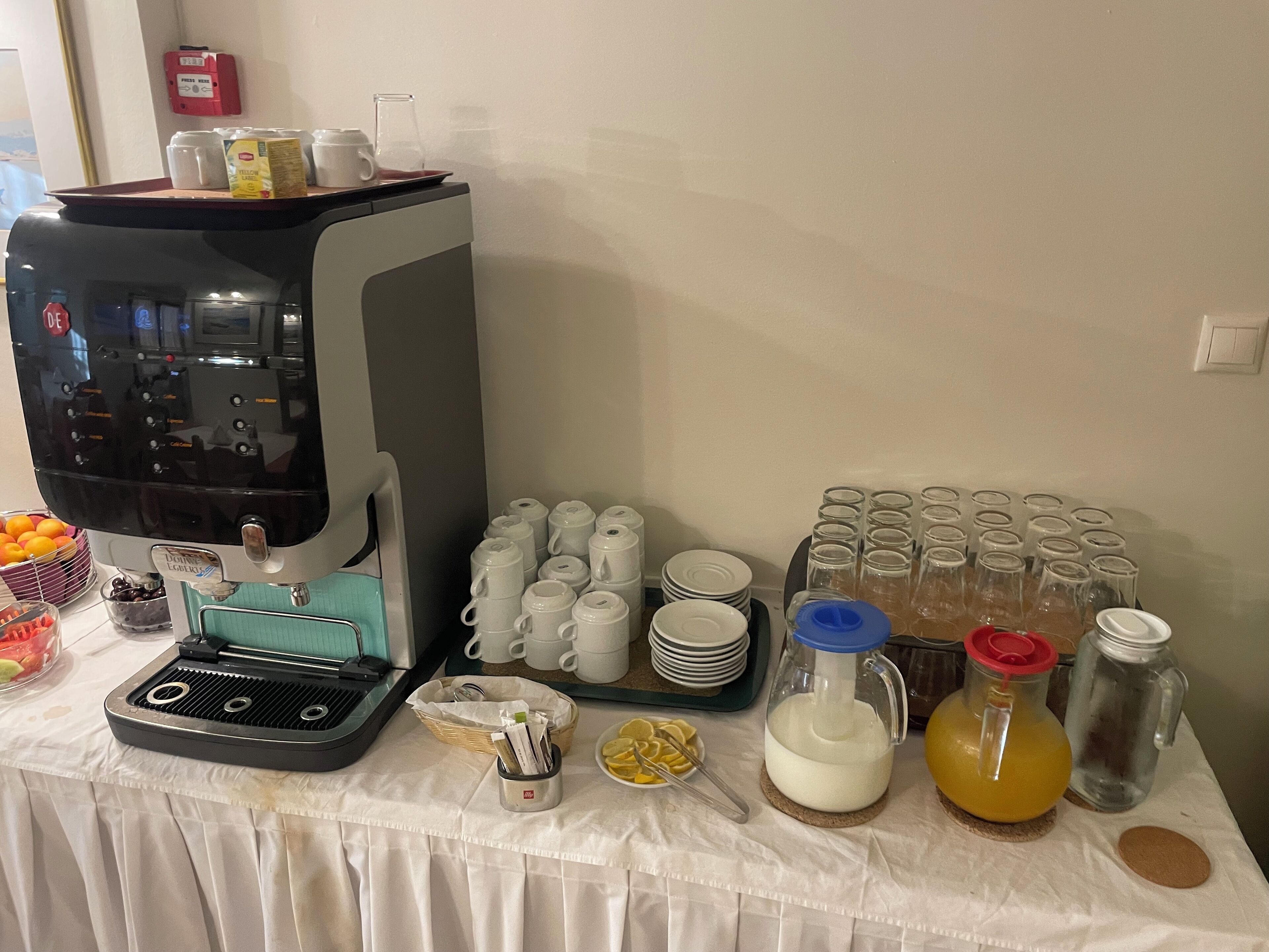 A breakfast setup with a coffee machine, milk jug, juice, and various cups and plates.
