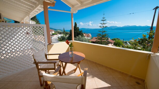 Varanda com vista para o mar e montanhas, mobiliário de madeira e painel de treliça branco.