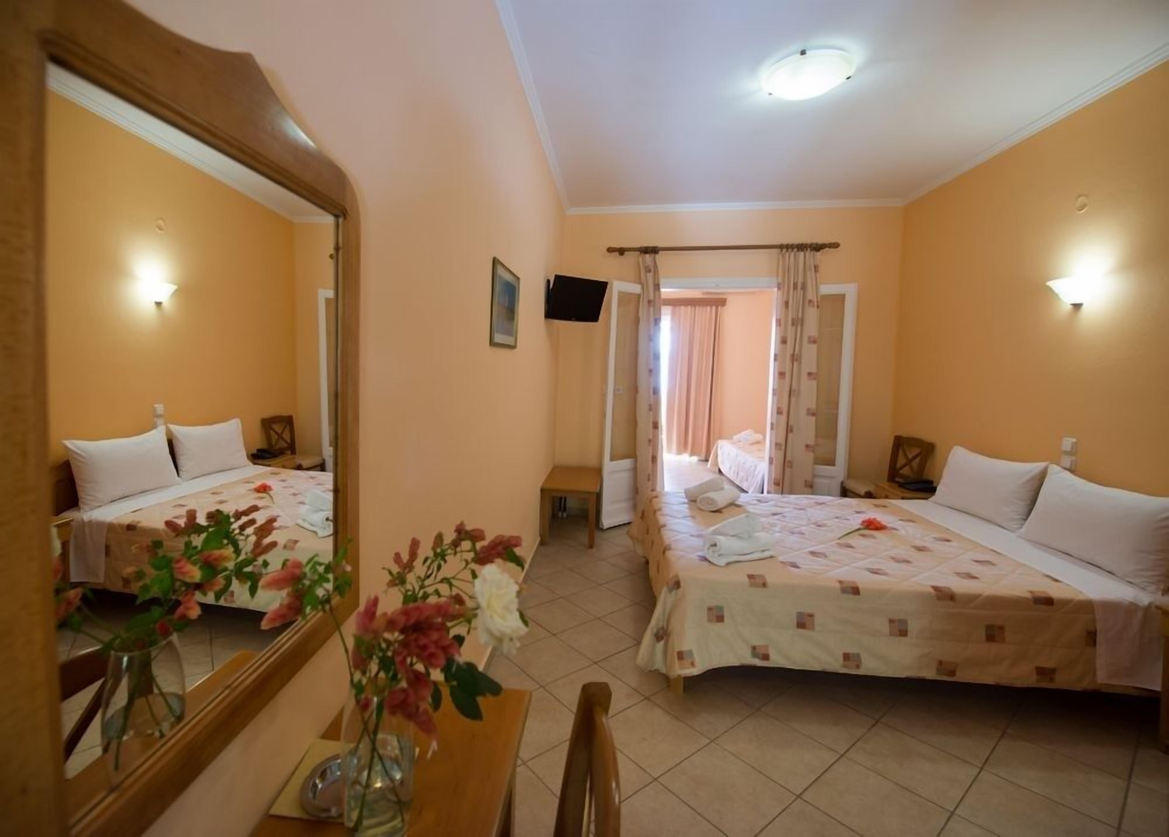 A hotel room with two beds, a mirror, a TV, and a vase with flowers.