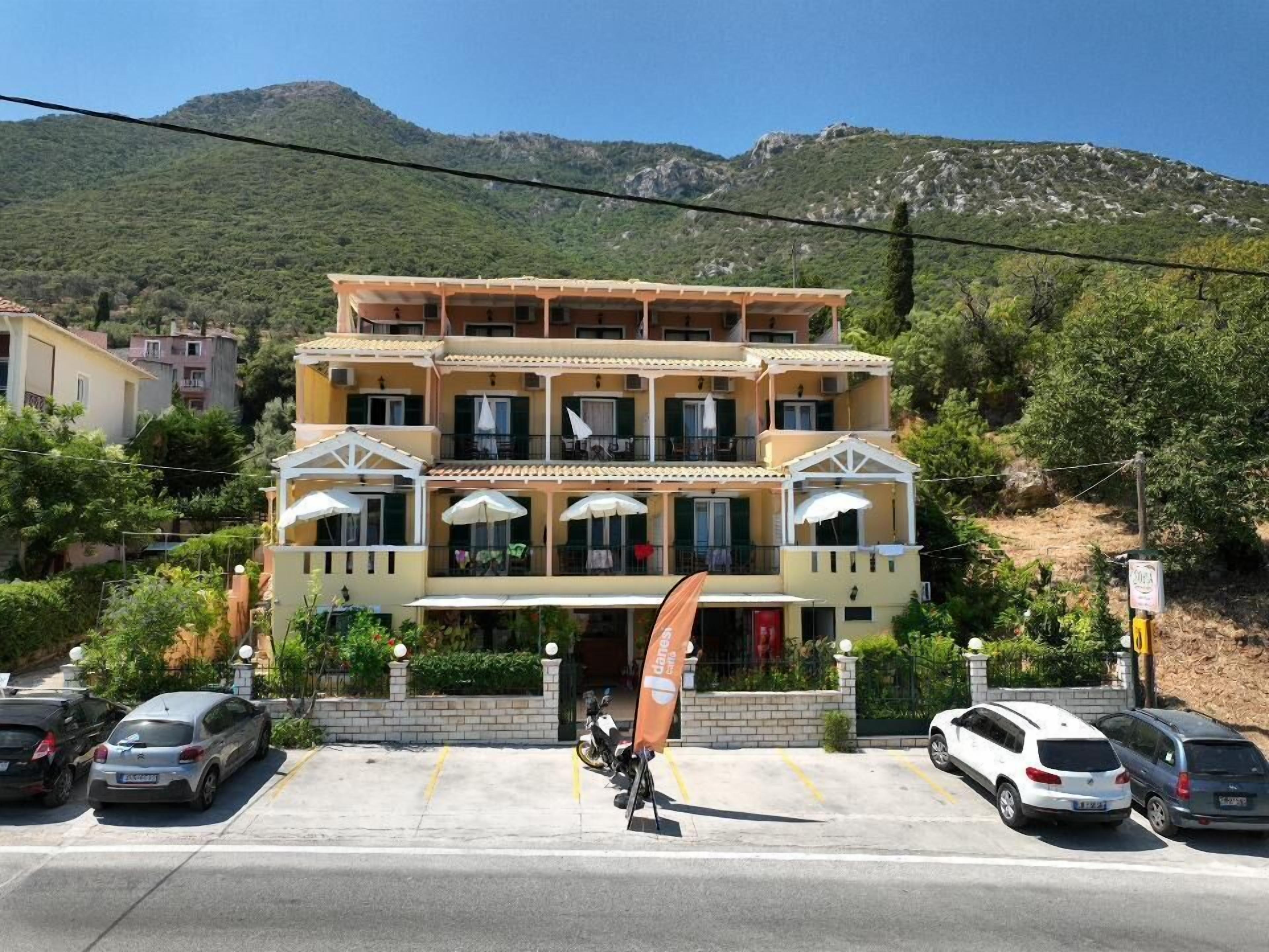 A multi-story hotel with balconies, a parking area, and a mountainous backdrop.