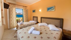 Quarto de hotel com duas camas, televisão, varanda vista para o mar e uma pequena mesa.