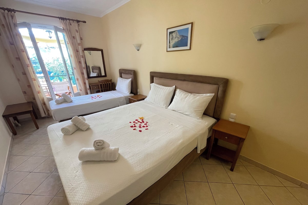A hotel room with two beds, a small table, a chair, a nightstand, and a window with curtains.