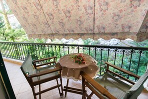 A balcony with a table and chairs, surrounded by a metal railing and lush greenery. - Hotel Sofia (Lefkada)