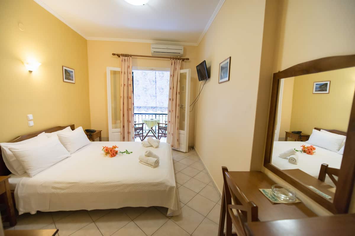 A hotel room with a bed, a desk, a chair, a TV, and a balcony with a table and chairs.