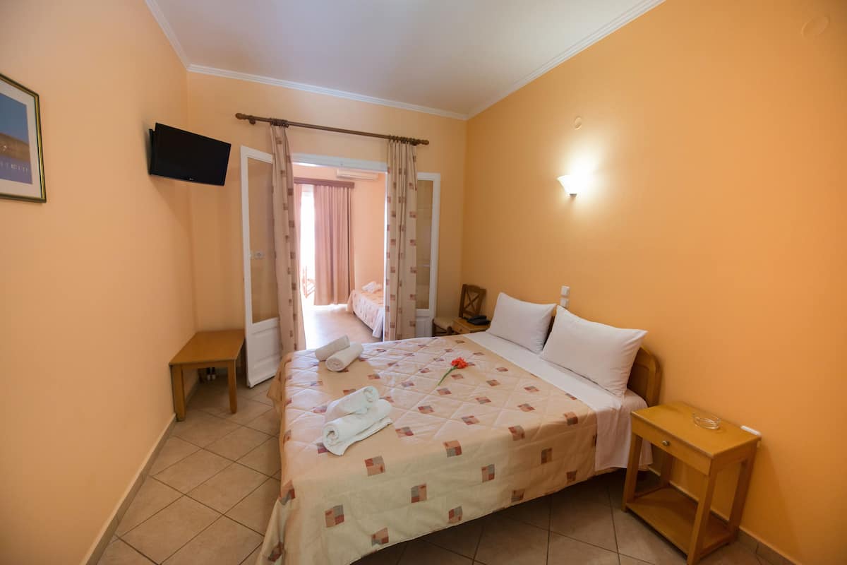 A hotel room with a bed, a bedside table, a TV mounted on the wall, and a door leading to another room.