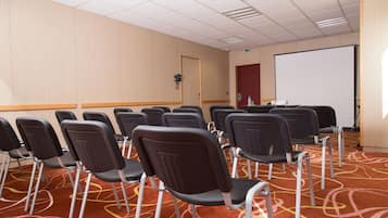 A conference room with rows of chairs, a projector screen, and a carpeted floor.