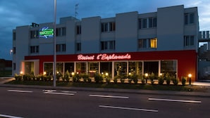 Een hotel met een rood-wit gevel, een neonbord en een goed verlichte ingang.